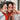 Three friends take a close selfie; center woman holds red heart glasses prop indoors